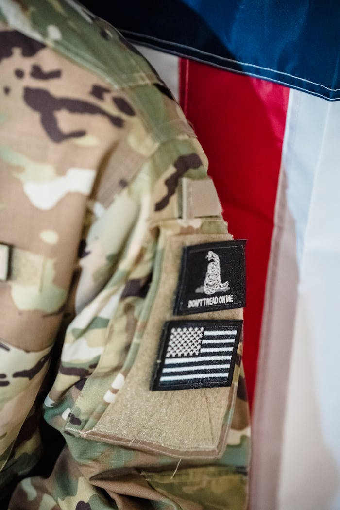 Home Close-up of a camouflage uniform featuring tactical patches in front of a flag.